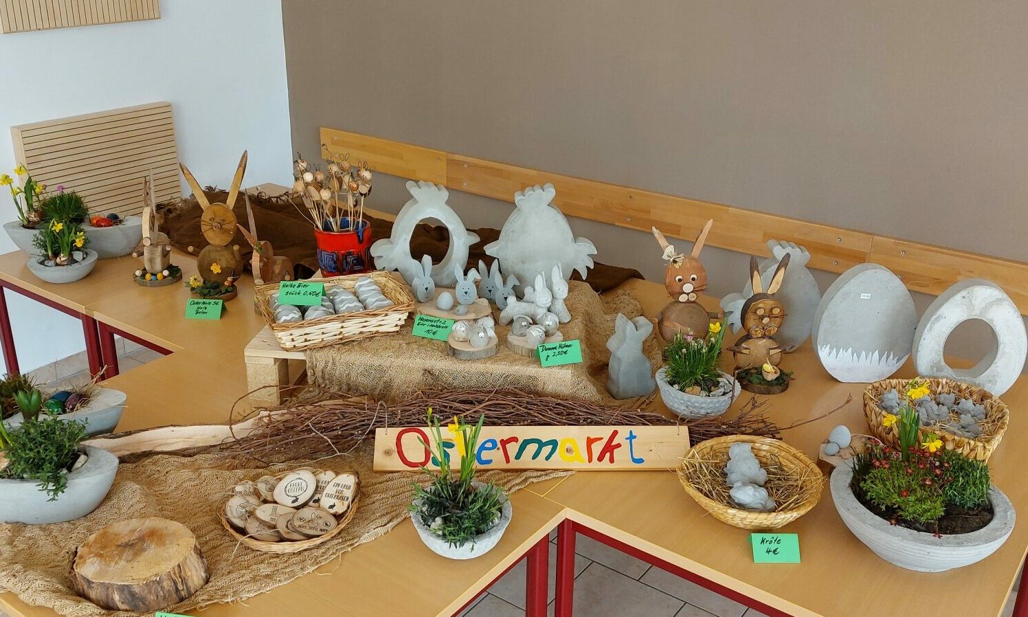 Ein Stand beim Ostermarkt in der Schule. Man sieht kleine Holscheiben in Ostereierform, welche graviert sind, kleine Hasenfiguren und kleine Pflanzgestecke, welche zum Verkauf stehen.