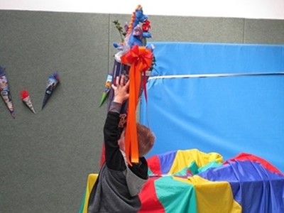 Ein Junge, welcher eine bunte Zuckertüte in die Luft hält. Der Junge ist von hinten zu sehen und durch die Bänderdeko auf der Zuckertüte fast vollständig verdeckt.